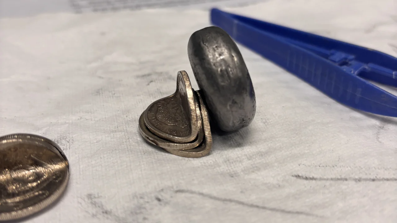 Cast alloy buttons next to a piece of graphite on paper, with the marks they leave when smeared